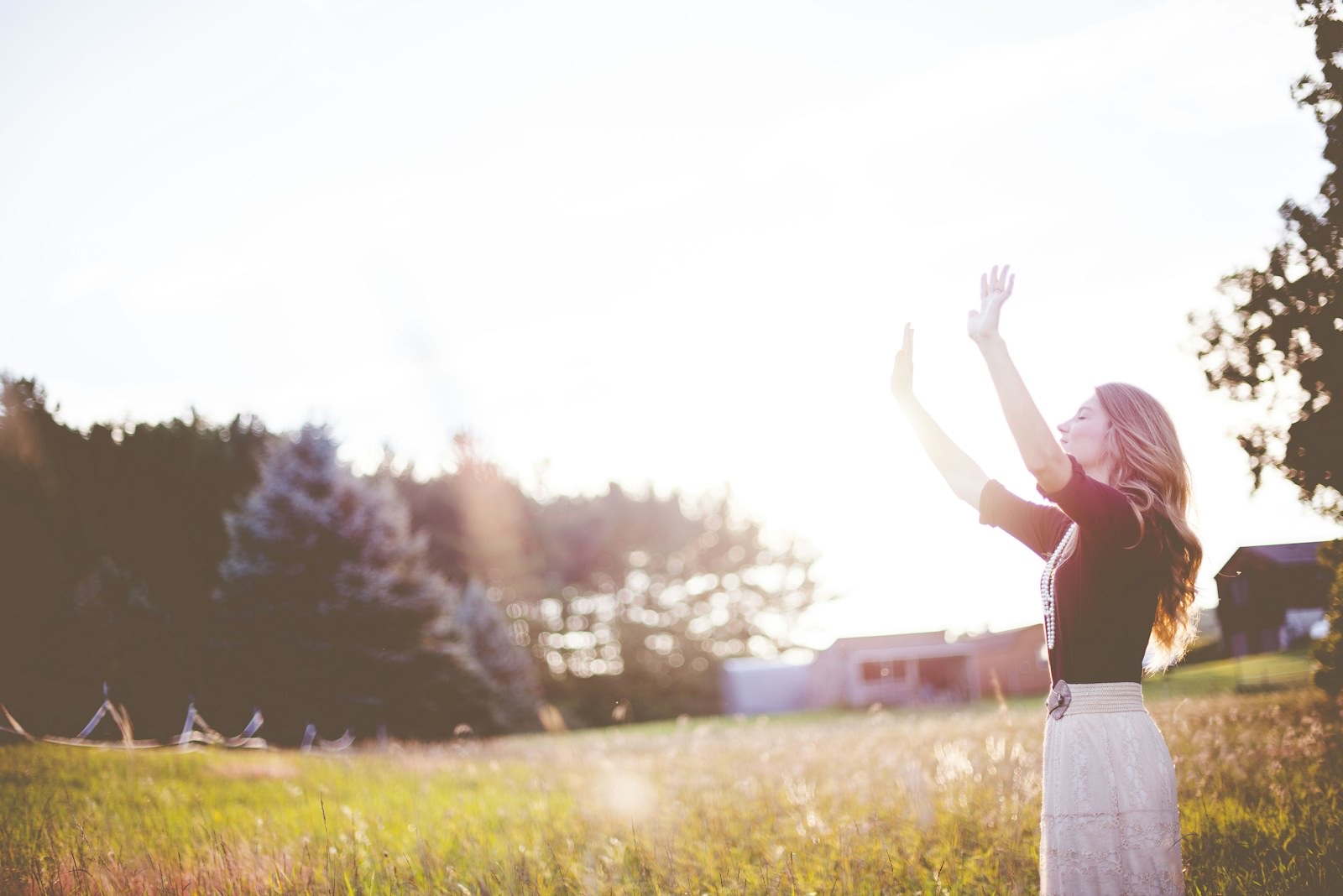 Woman with her hands raised in front of an open green field