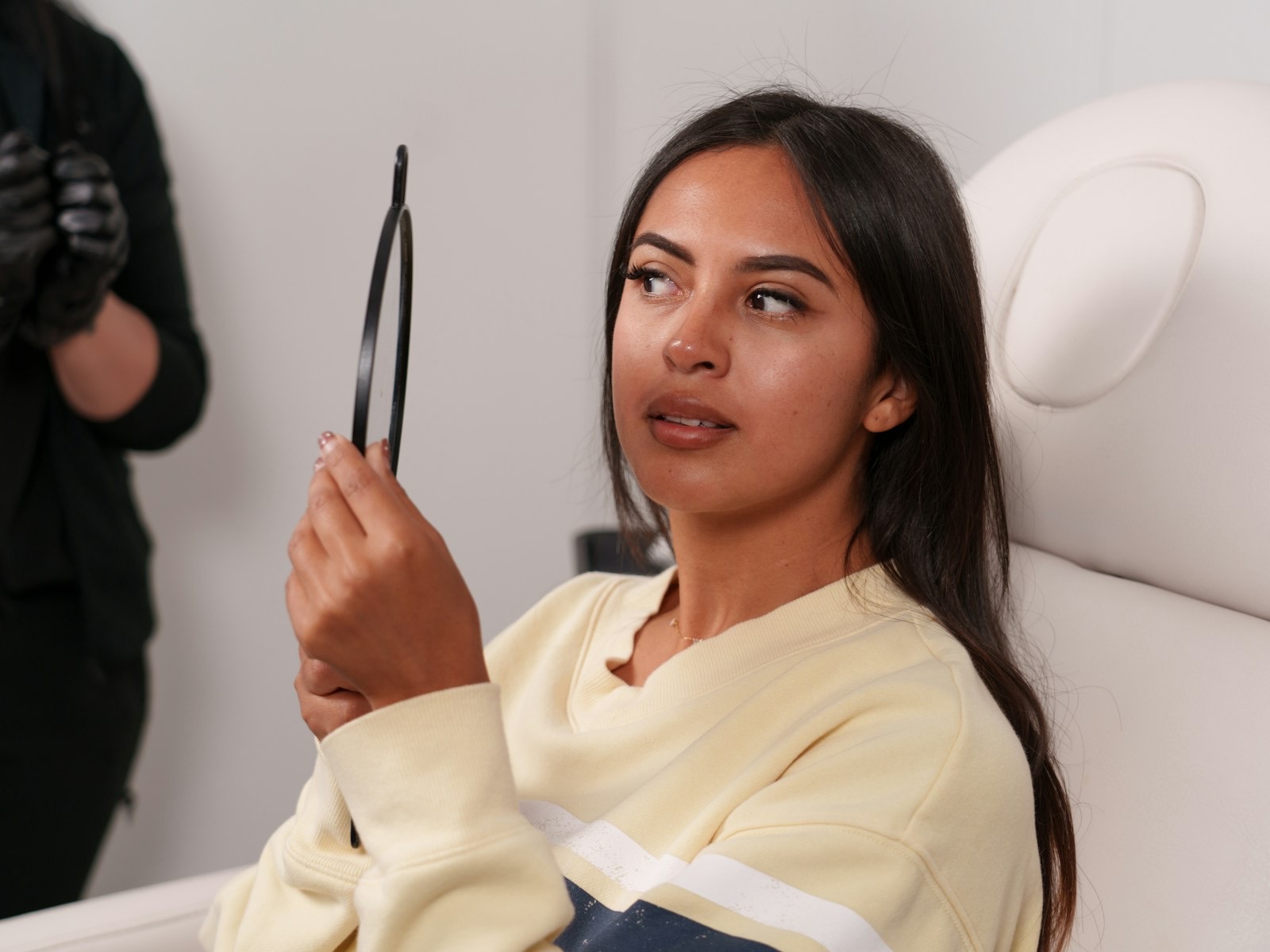 A young woman looks in a handheld mirror while sitting