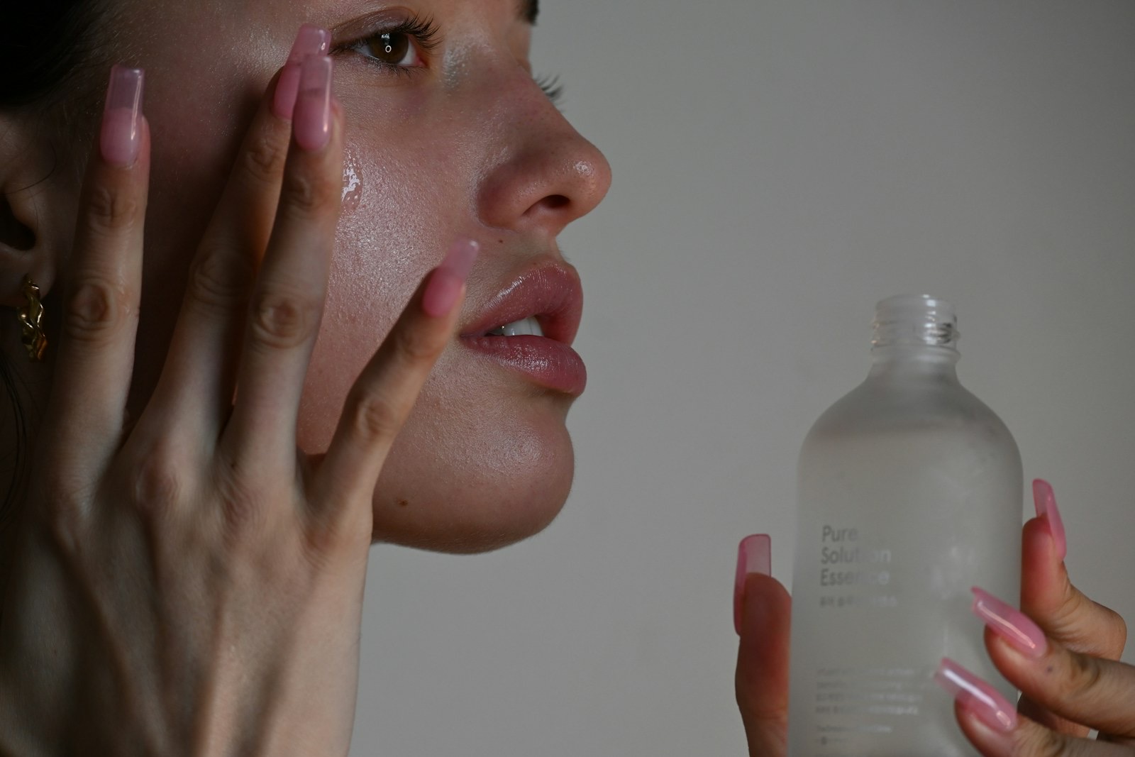 A person applying serum to their cheek with long pink nails