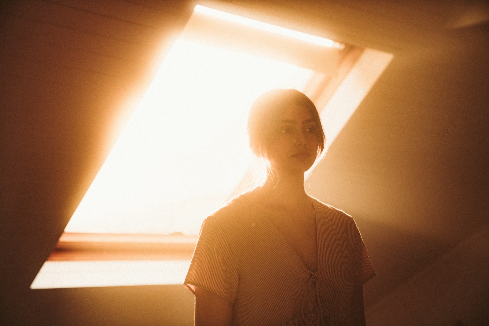 Woman in a white knit sweater standing beside a window in daylight